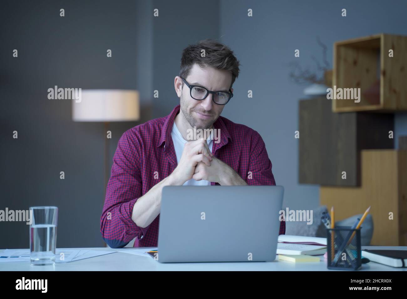 Il giovane dipendente tedesco dell'ufficio domestico pensivo siede alla scrivania sul posto di lavoro opera online su un laptop Foto Stock
