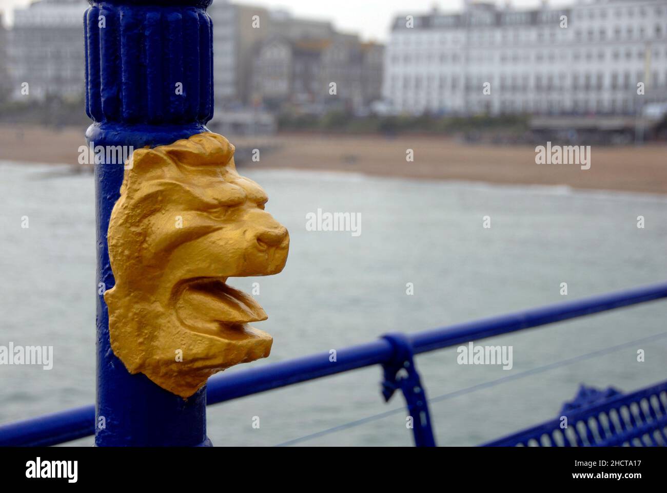 Testa di leone decorativa dipinta d'oro sul posto sul molo di Eastbourne, East Sussex, Inghilterra, con hotel sul lungomare oltre Foto Stock