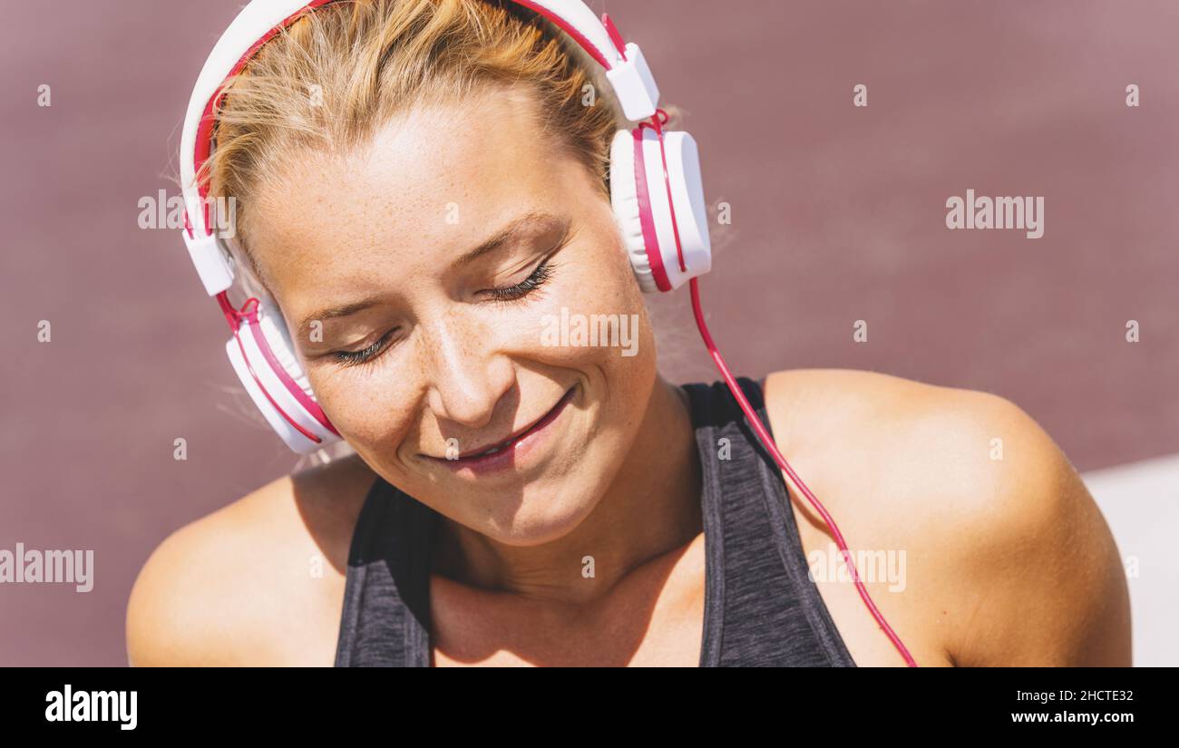 Giovane donna che ascolta musica con le cuffie per motivazione fitness. Ritratto di una giovane donna in sportswear seduta rilassante ottenere ispirato. Foto Stock