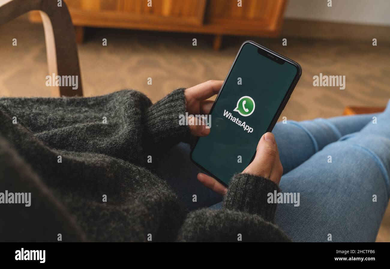 Donna con un iPhone X che apre l'app Whatsapp in salotto. WhatsApp Messenger per l'invio di messaggi via Internet. Foto Stock