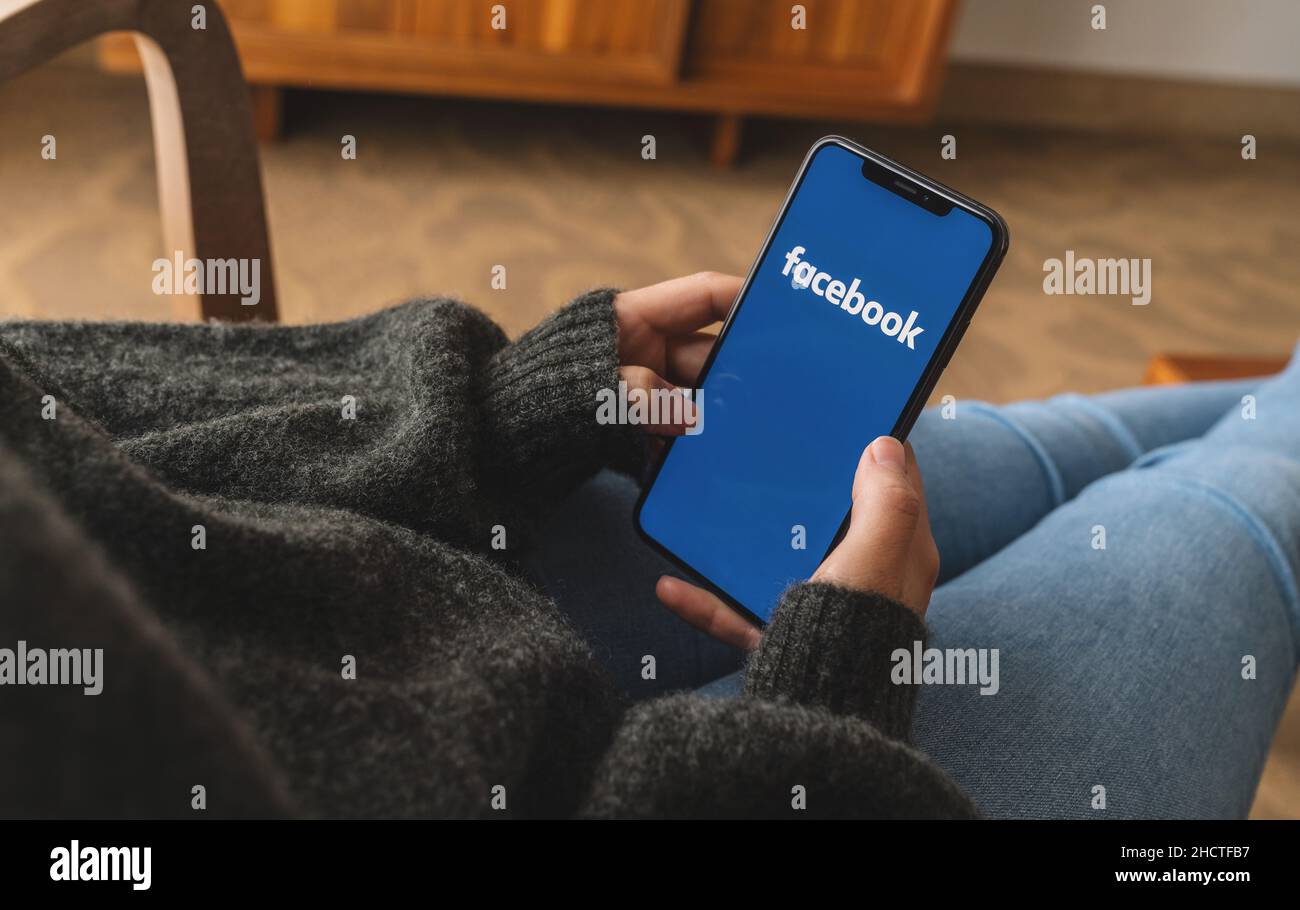 Donna che tiene in mano iphone X con il logo dell'applicazione Facebook in un ambiente di vita. Facebook è un servizio di social networking online fondato nel febbraio 20 Foto Stock