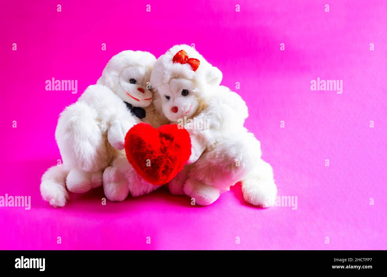 Scimmie giocattolo morbide che tengono un cuore su uno sfondo rosa. Un simbolo d'amore, San valentino Foto Stock