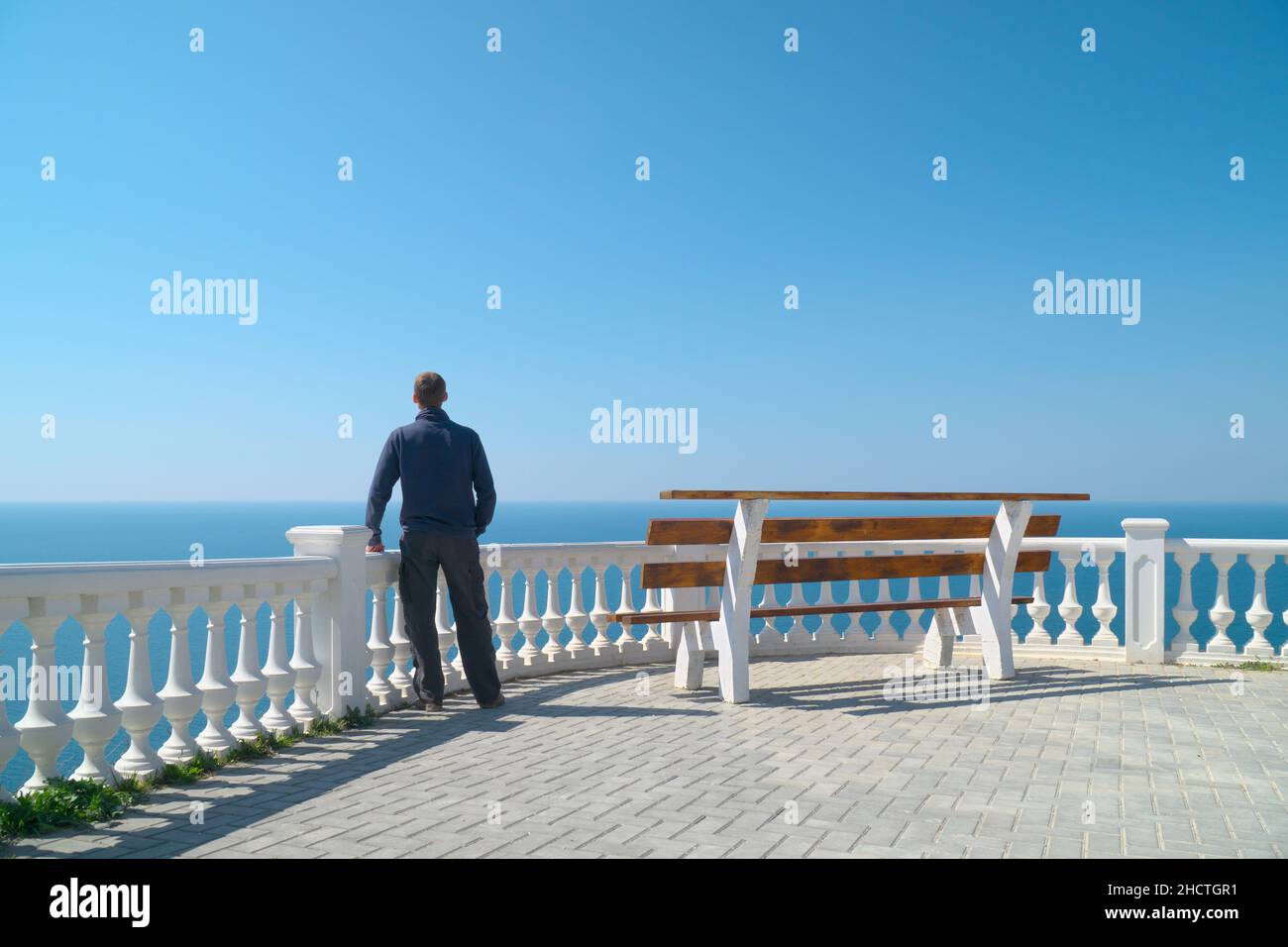 Uomo in piedi sul balcone e guardare l'orizzonte del mare di giorno. Calma e relax composizione. Foto Stock