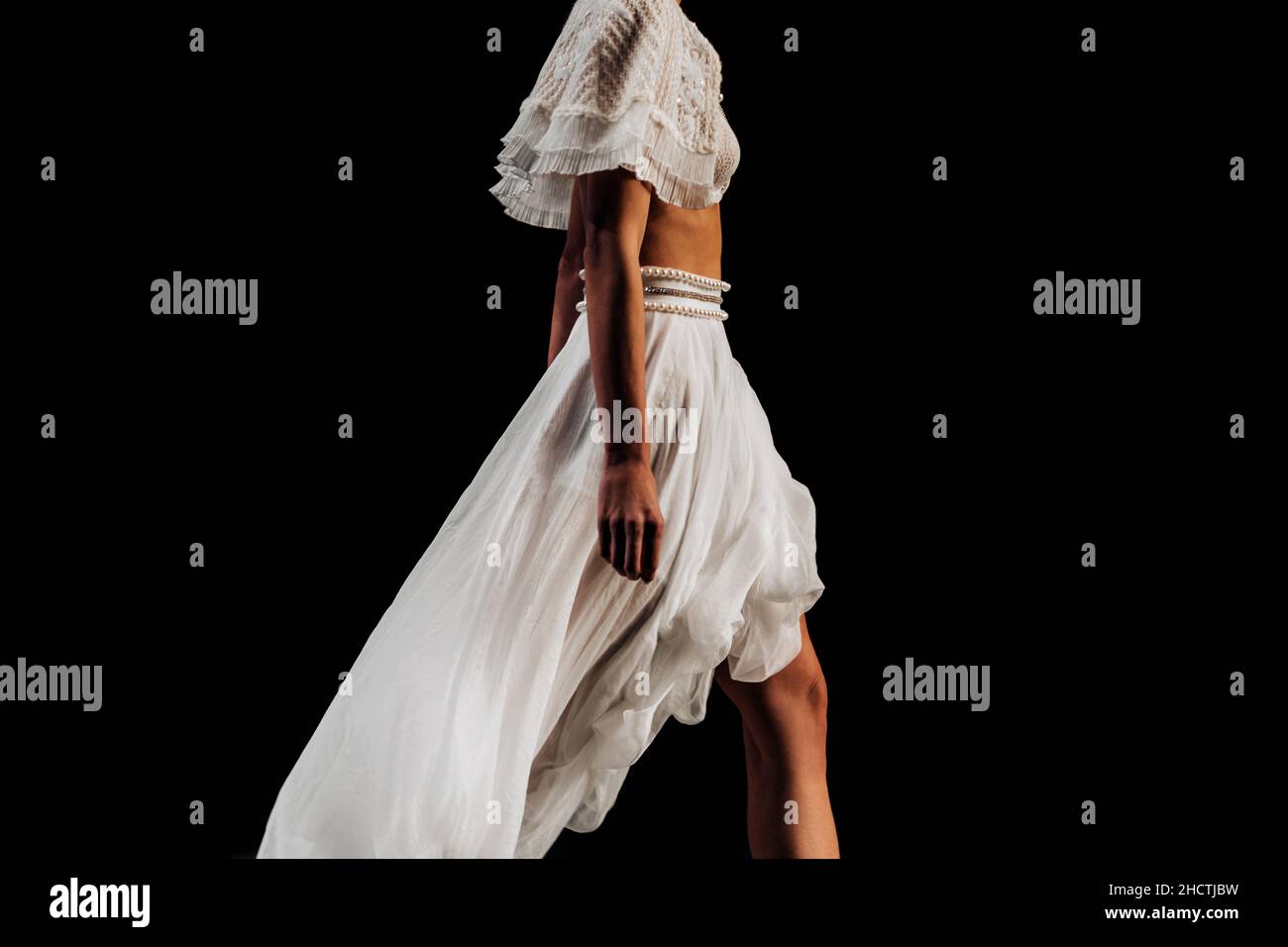 Figura ritagliata di un modello alla moda che cammina lungo la passerella in un abito bianco firmato su sfondo nero. Dettagli della settimana della moda Foto Stock