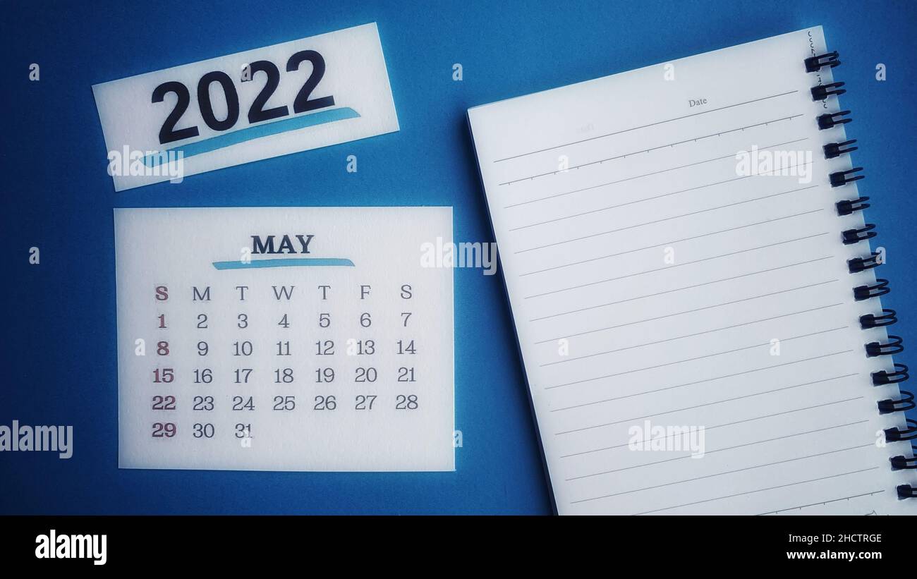 Calendario bianco di maggio 2022 con blocco note e sfondo blu. Foto Stock