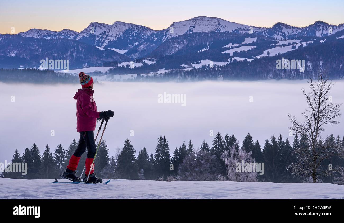 Paesaggio con donna che guarda l'alba sulla catena montuosa di Nagelfluh durante un'escursione con racchette da neve nelle Alpi di Allgaeu vicino a Oberstaufen, Germania, Baviera, Foto Stock