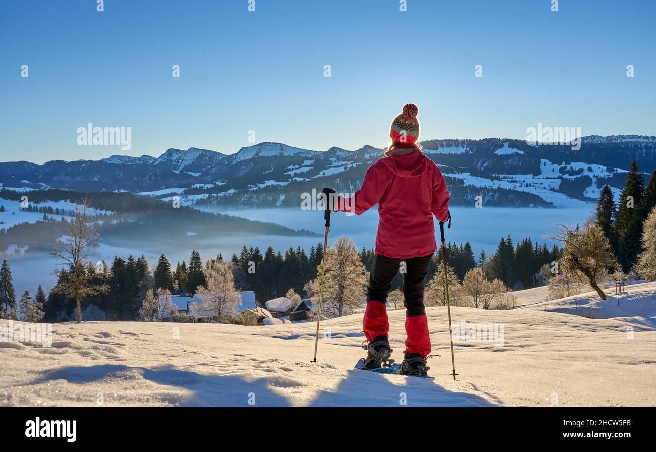 Paesaggio con donna che guarda l'alba sulla catena montuosa di Nagelfluh durante un'escursione con racchette da neve nelle Alpi di Allgaeu vicino a Oberstaufen, Germania, Baviera, Foto Stock