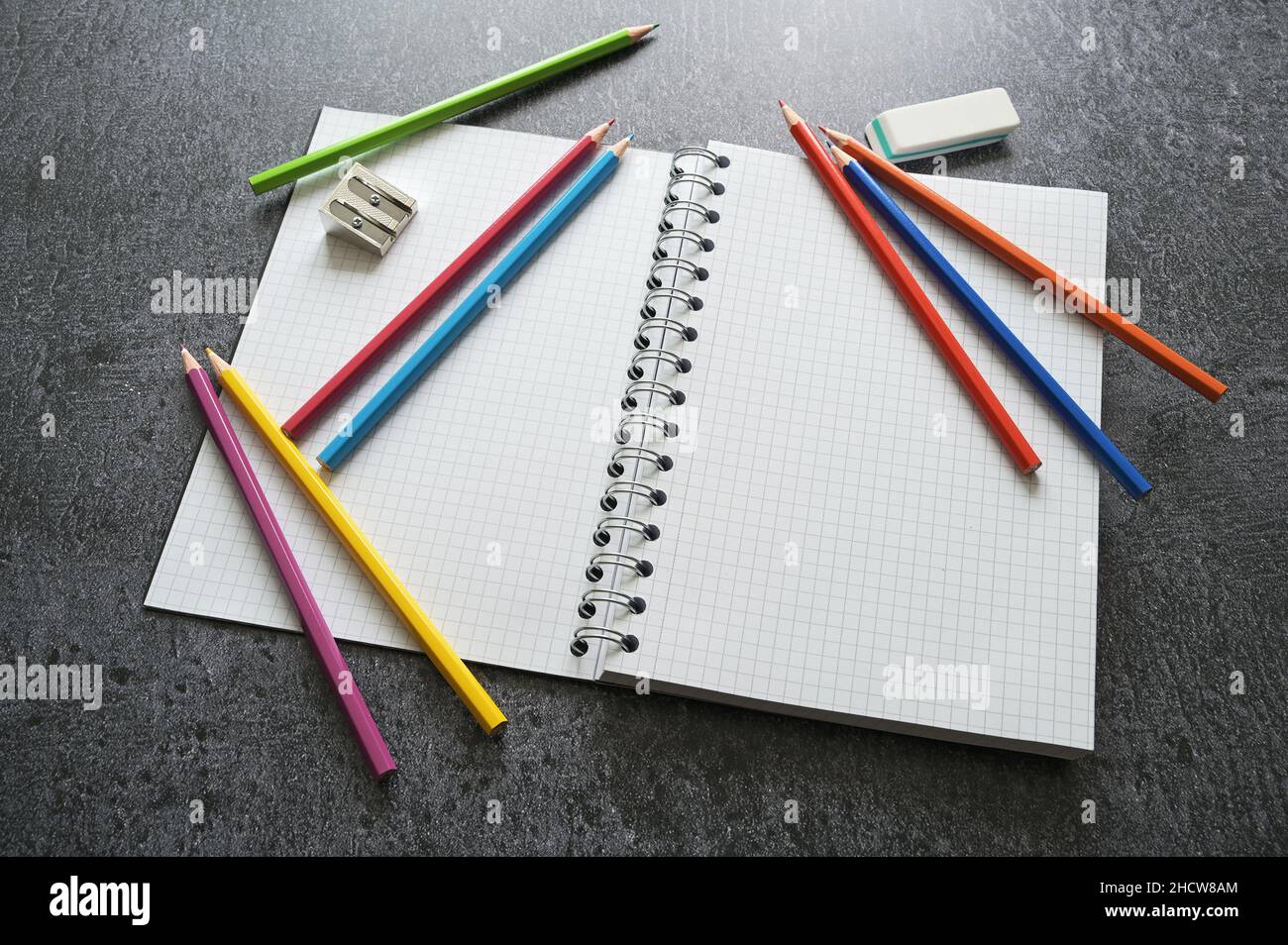 Scrivania per il lavoro creativo con un notebook vuoto a spirale, pastelli, affilatrice e gomma su un tavolo grigio scuro, spazio di copia, messa a fuoco selezionata, profondità ridotta Foto Stock