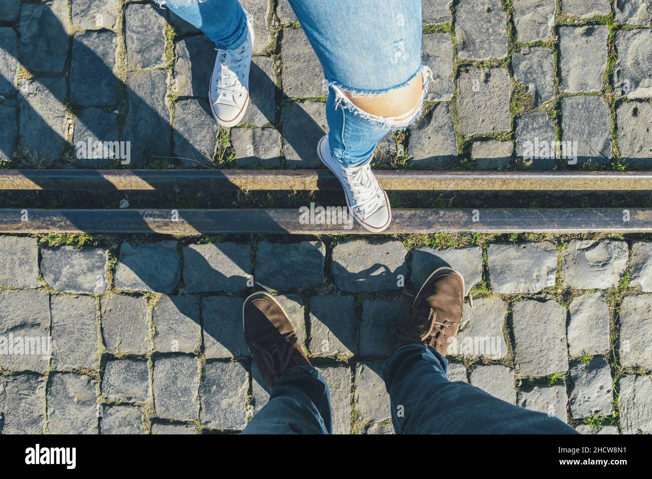 il giovane uomo e una ragazza in sneakers si trova di fronte su ciottoli su una pista di treno, footsie ad angolo alto o flortrait, personale pespettivo dall'alto. Foto Stock