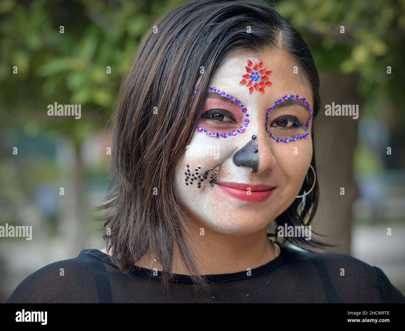 Giovane bella messicana caucasica donna con dipinto tradizionale viso make-up guarda spettatore durante il festival del giorno dei morti (dia de los Muertos). Foto Stock