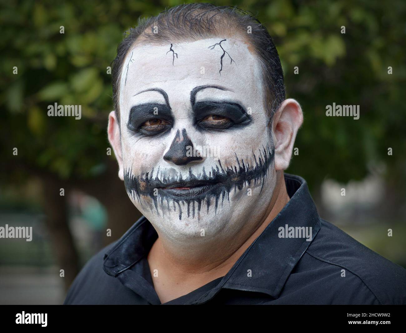 L'uomo caucasico messicano di mezza età con il make-up del volto dipinto di bianco simile a zombie guarda lo spettatore il giorno dei morti (dia de los Muertos). Foto Stock