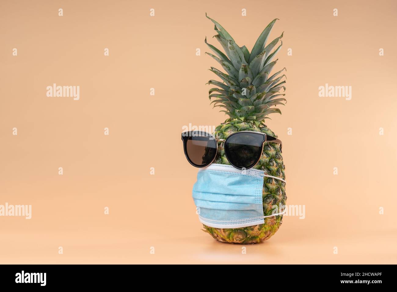 Interpretazione della frutta di ananas in forma umana durante una pandemica indossare occhiali da sole e una maschera di protezione medico. Spazio di copia su sfondo giallo Foto Stock