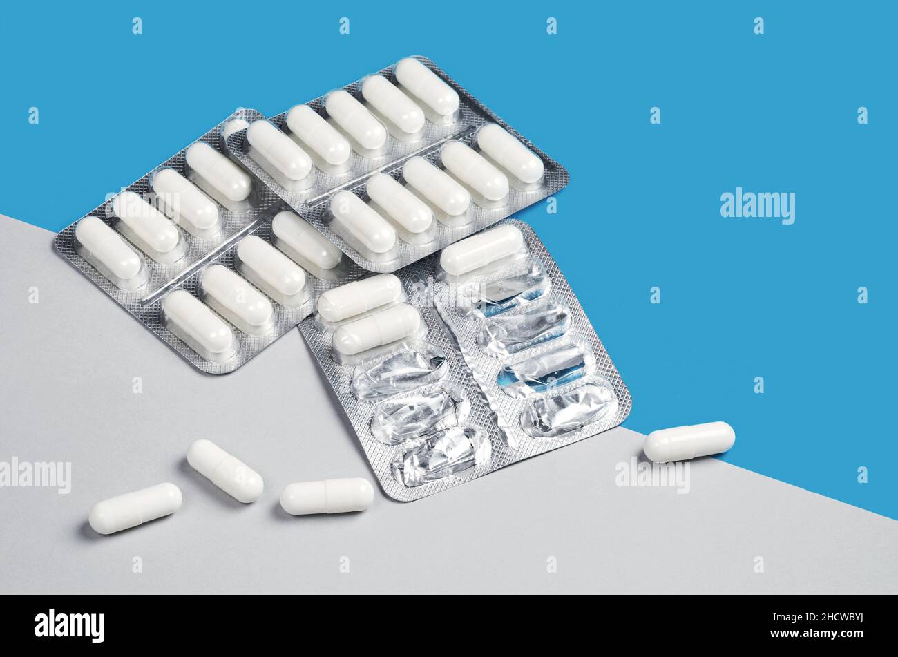 Capsule bianche confezionate in blister su sfondo grigio e blu. Tema della medicina e della salute Foto Stock