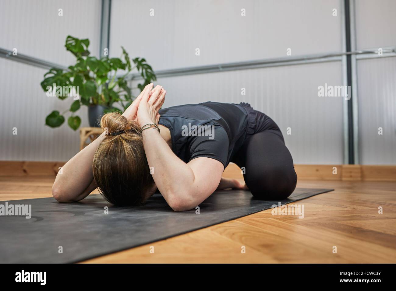 Rilassato barefoot femmina chiudere gli occhi e gesturing Gyan mudra mentre si siede su tappeto in posa di loto e meditating durante la sessione di yoga in studio luce Foto Stock