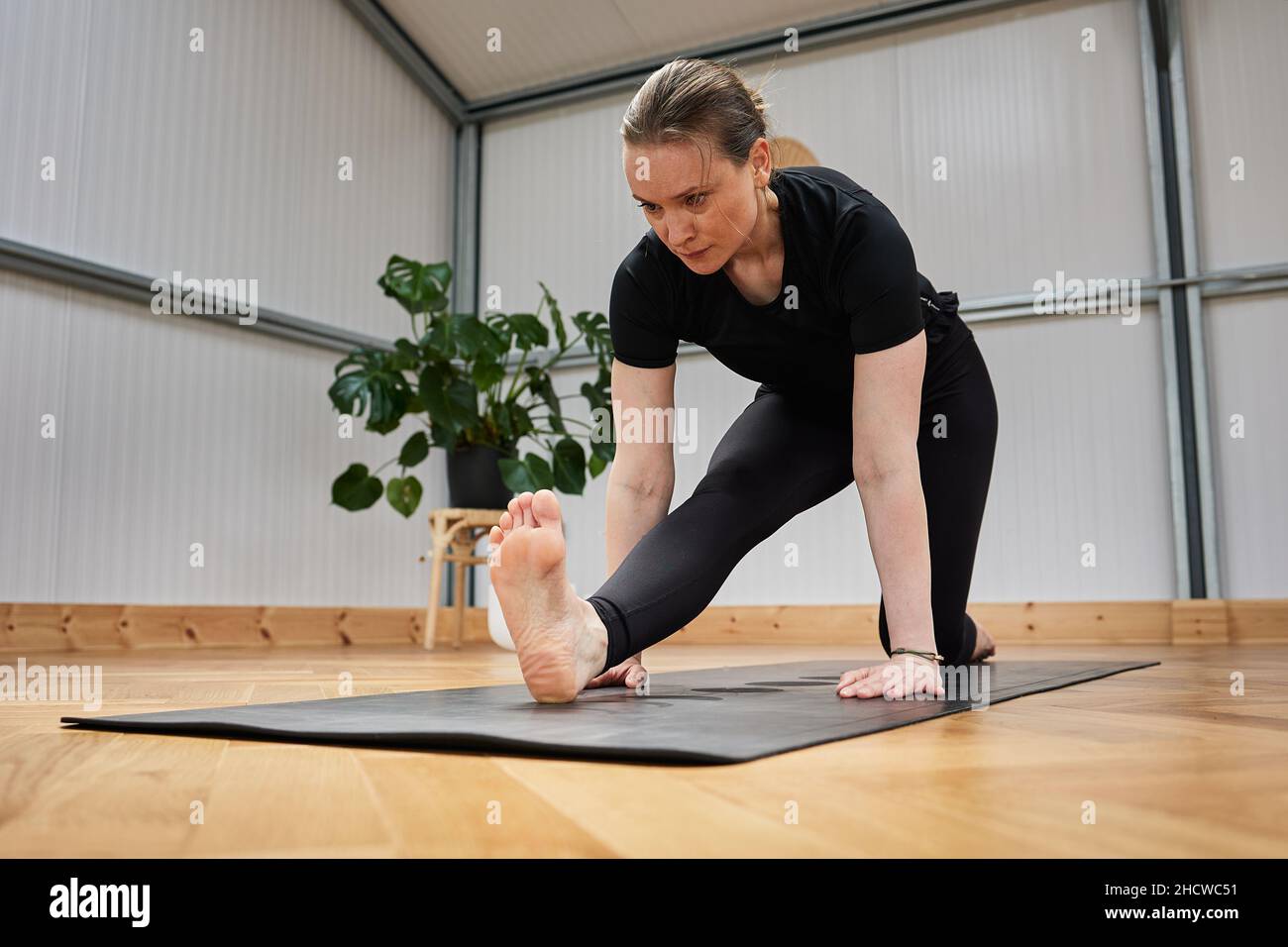 Rilassato barefoot femmina chiudere gli occhi e gesturing Gyan mudra mentre si siede su tappeto in posa di loto e meditating durante la sessione di yoga in studio luce Foto Stock