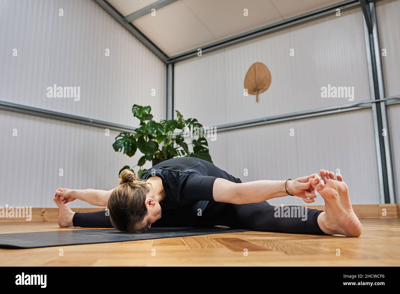 giovane donna con grande flessibilità che tocca le dita dei piedi con le mani su un tappetino yoga Foto Stock