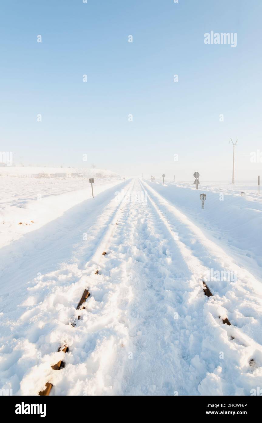 Piste ferroviarie quasi innevate, dopo una nevicata, in una mattinata di sole, con un punto di fuga verso l'orizzonte. Immagine verticale. Nevicate un Foto Stock