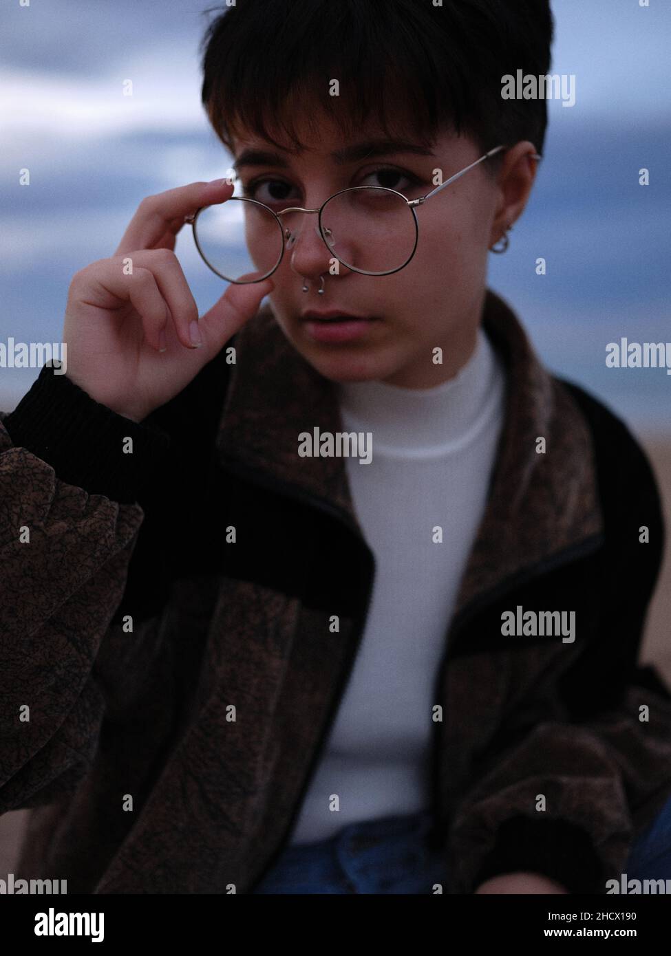 giovane donna trans che prende i suoi occhiali mentre guarda con intelligenza la macchina fotografica Foto Stock