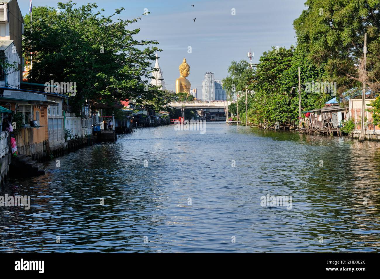 Klong Bangkok Yai, un canale a Thonburi, Bangkok, Thailandia, Thonburi una volta la capitale del vecchio Siam; b/g: Il Buddha gigante di Wat Paknam Phasi Charoen Foto Stock