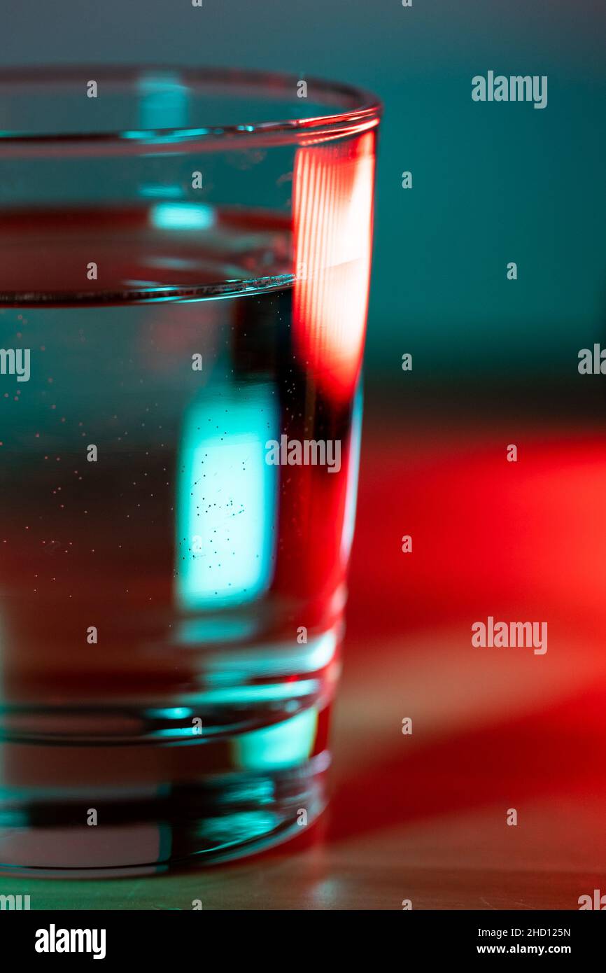 Macro scatto di vetro d'acqua in rosso blu luce neon trendy. Foto Stock
