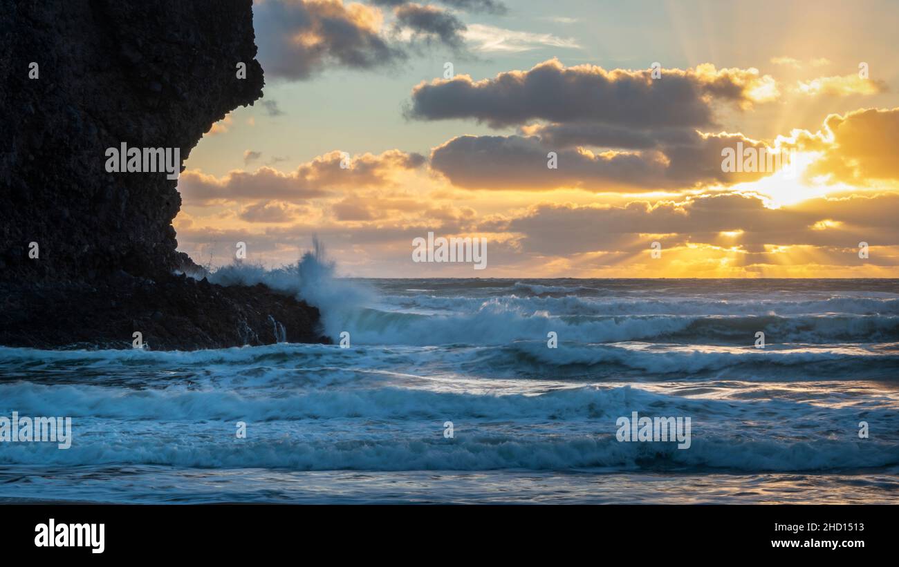 Enormi onde che si infrangono contro le rocce alla spiaggia di Piha al tramonto, Auckland, Nuova Zelanda. Foto Stock