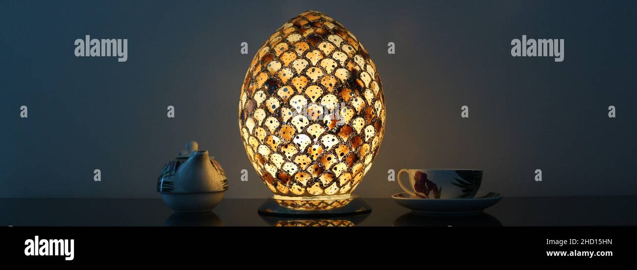 La luce di una lampada ovale risplende e si riflette su una teiera e un teacup. Foto Stock