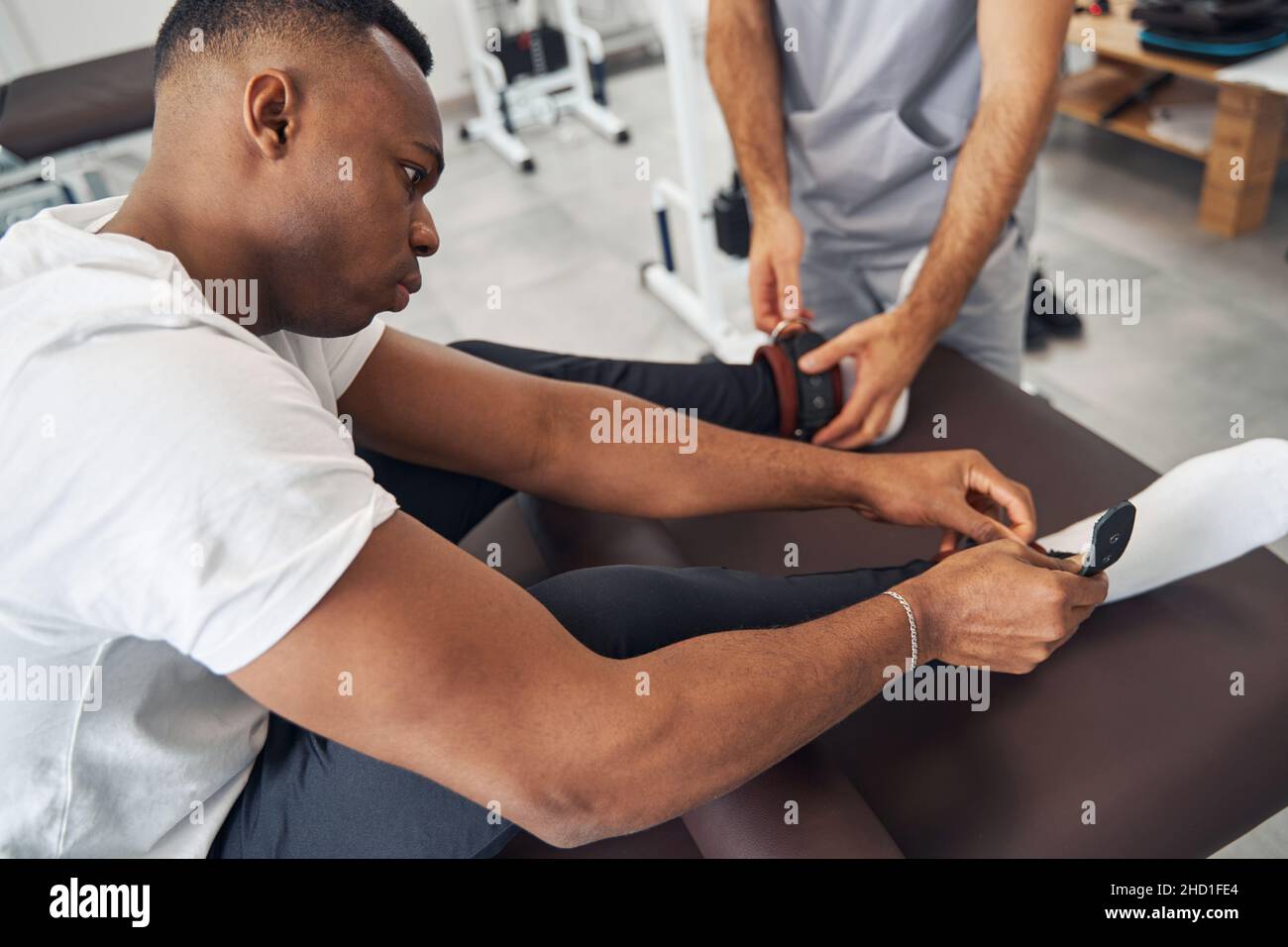 Uomo che mette pesi sulle caviglie assistito dal fisioterapista Foto Stock