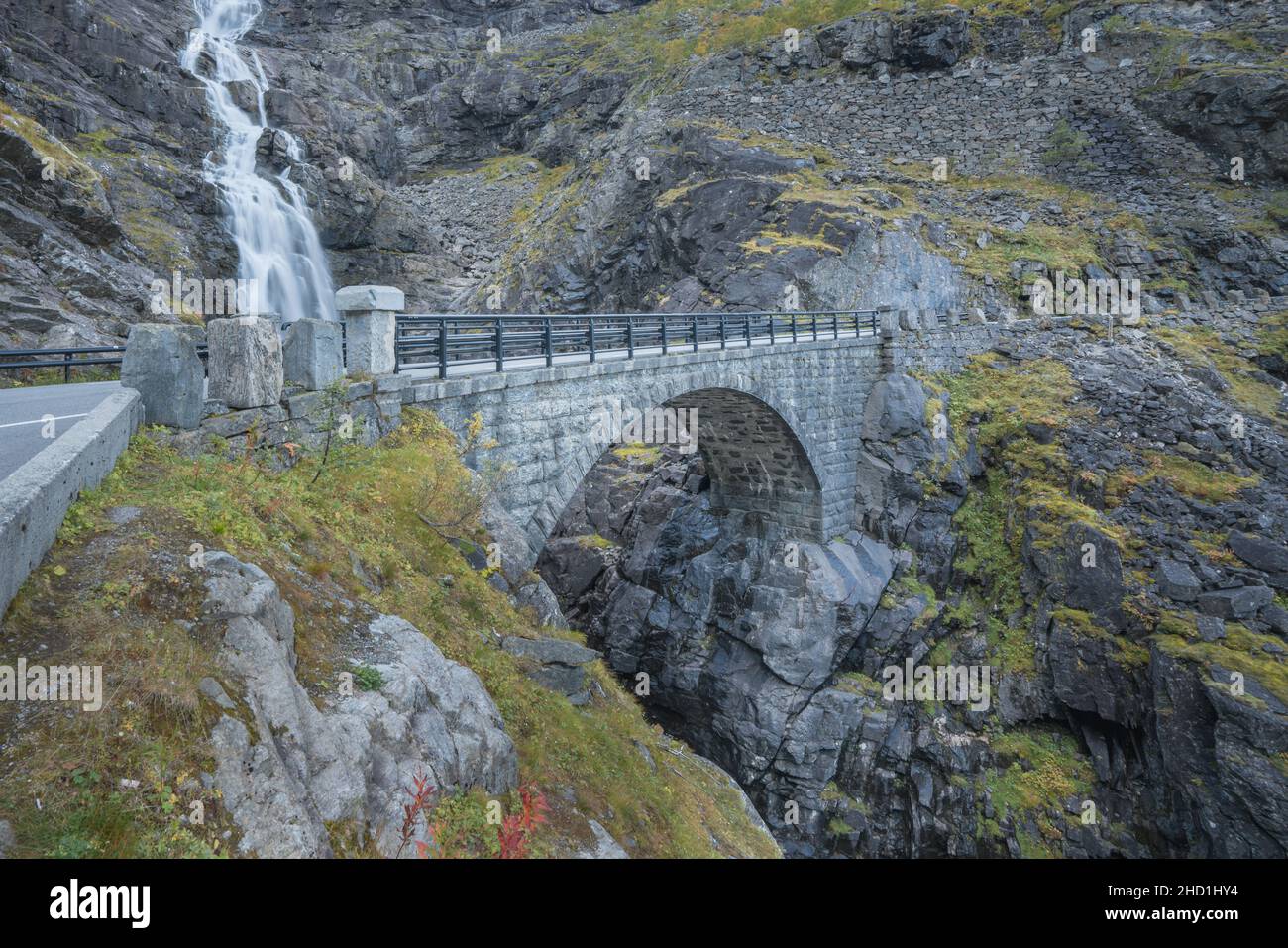 Stretto ponte di pietra sulla serpentina della famosa strada di montagna Troll Stigen, o Trollstigen, in Norvegia. Cascata Stigfossen sul retro. Foto Stock