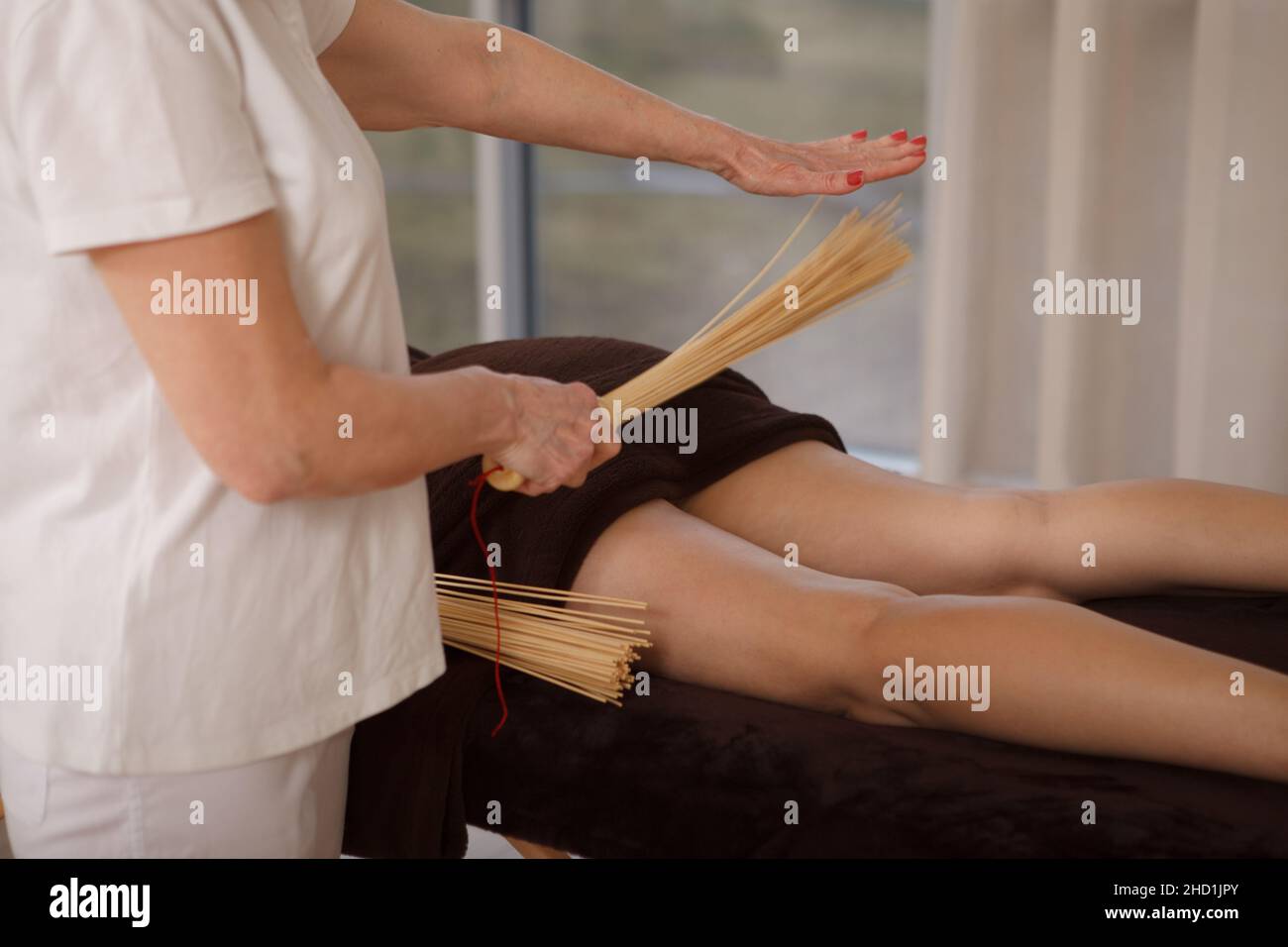 Donna irriconoscibile che ottiene il massaggio completo del corpo con la scopa del massaggio di bambù al centro termale Foto Stock