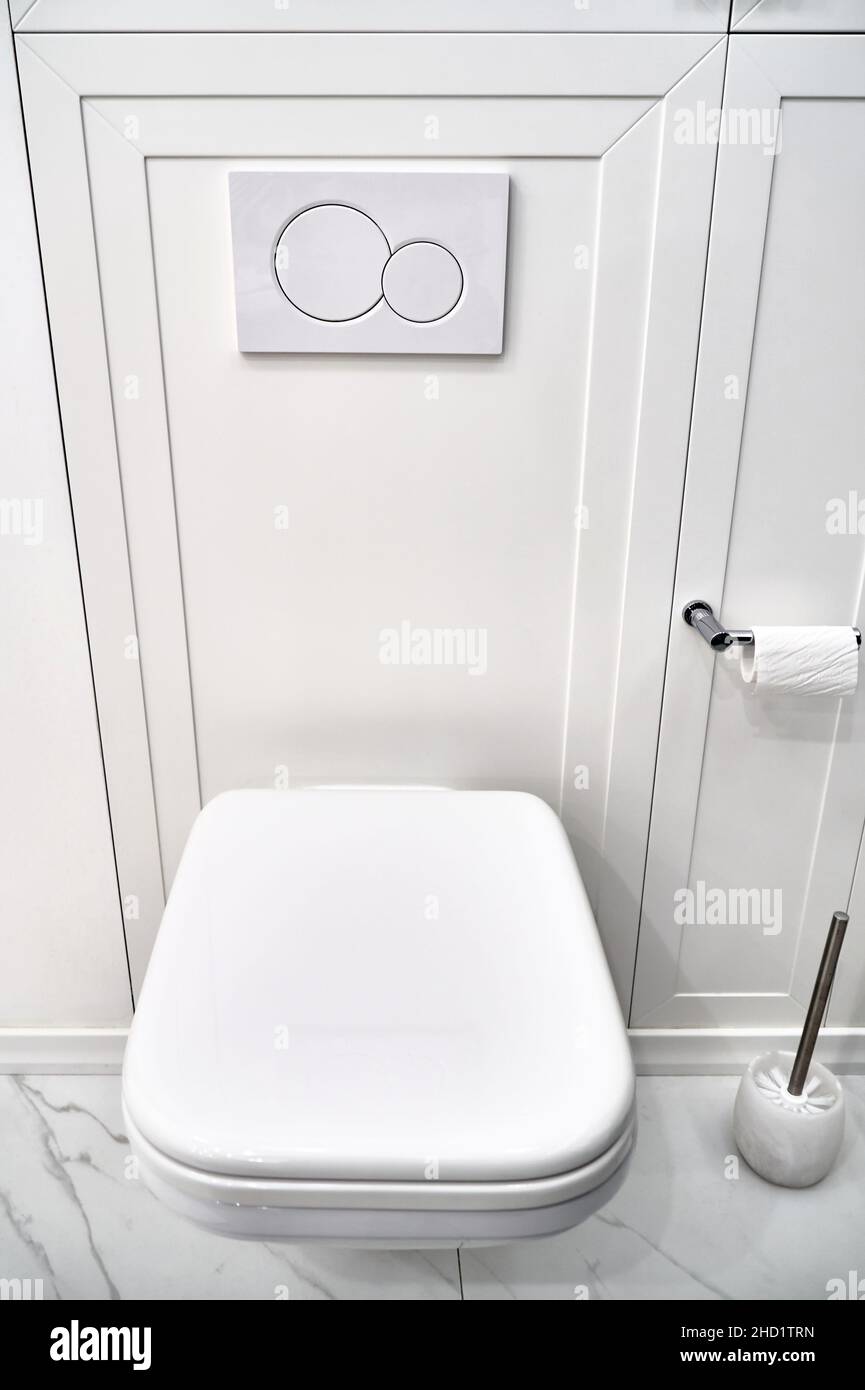 Elegante WC contemporaneo con vasca nascosta dietro il pannello bianco e pulsanti a filo a parete in luce stanza da bagno vista ravvicinata Foto Stock