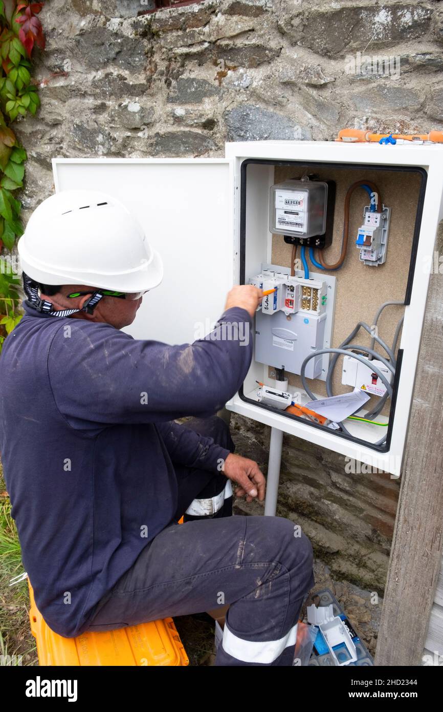 Ingegnere elettrico uomo di lavoro che collega nuove linee elettriche residenziali alimentazione cablaggio installazione misuratore in armadio Galles UK KATHY DEWITT Foto Stock