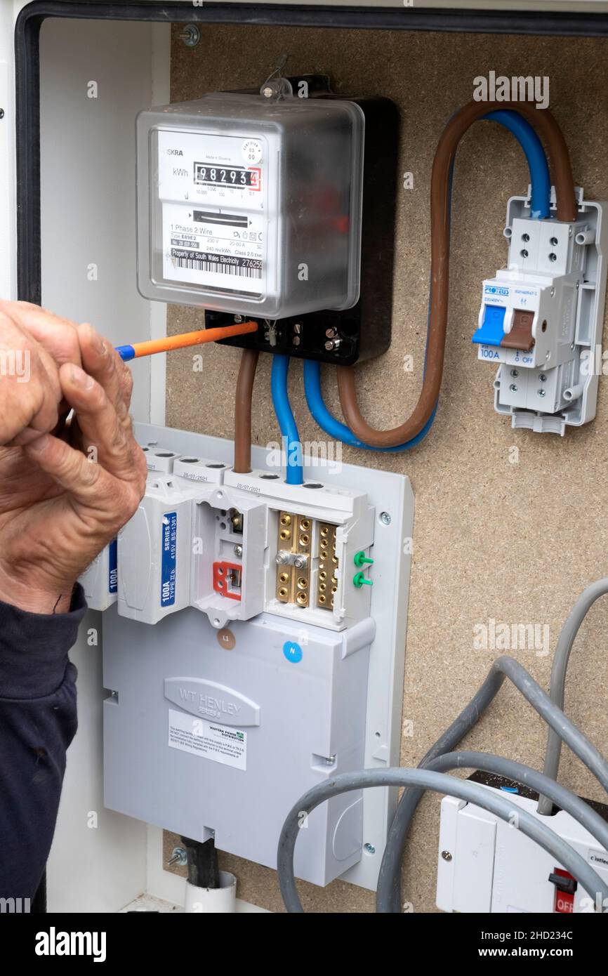 Ingegnere elettrico uomo di lavoro che collega nuove linee elettriche residenziali alimentazione cablaggio installazione misuratore in armadio Galles UK KATHY DEWITT Foto Stock