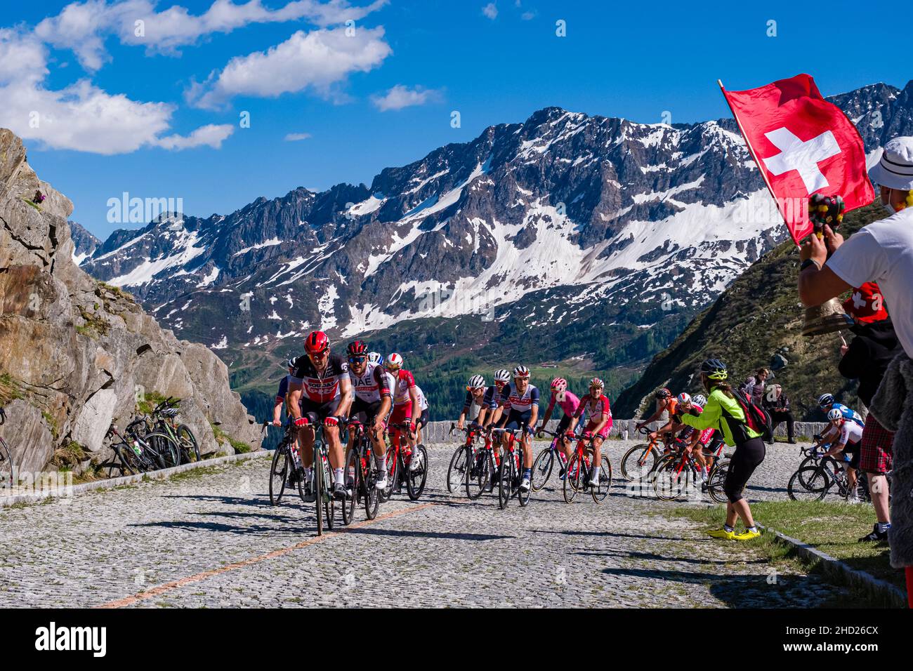 Un gran gruppo di ciclisti che corre sulla Tremola San Gottardo al Tour de Suisse 2021, circondando montagne innevate. Foto Stock