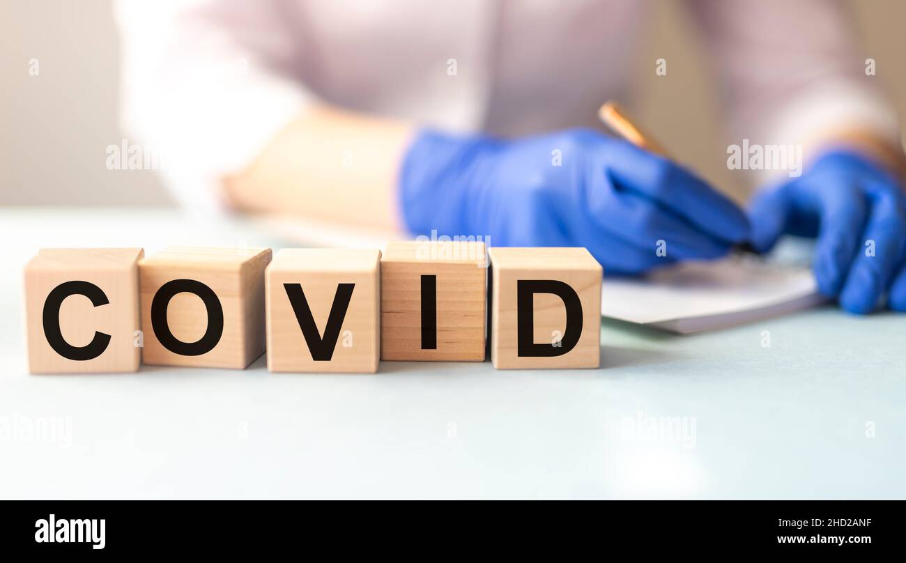 Parola COVID sui blocchi di cubo sul tavolo luminoso con mano del medico sfocante sullo sfondo Foto Stock