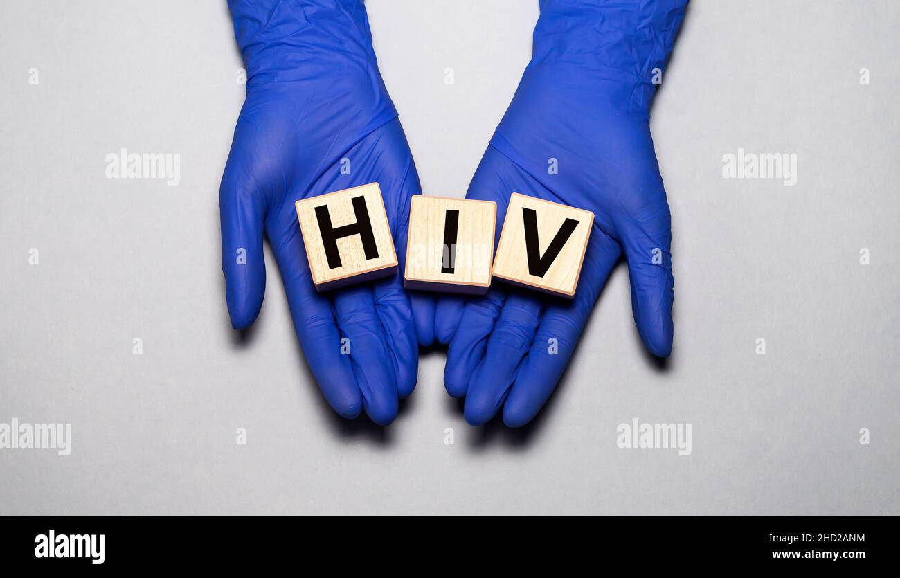 Le mani del medico nei guanti medici tengono i blocchi di legno del cubo del virus di immunodeficienza umana dell'HIV Foto Stock