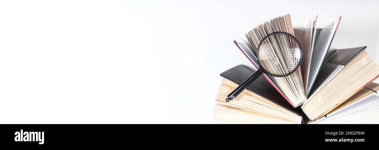 Lente di ingrandimento sopra il libro di carta aperto. Concetto di conoscenza, ricerca e studio. Banner con spazio di copia. Foto Stock