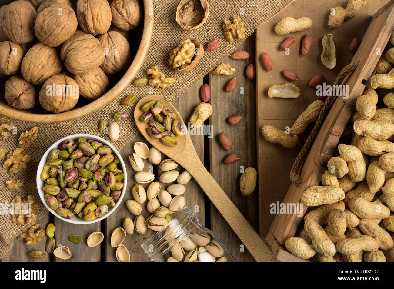 Noci e ciotole diverse da vicino su un tavolo di legno e sfondo marrone. Arachidi, noci, anacardi, mandorle, nocciole, pistacchio Foto Stock