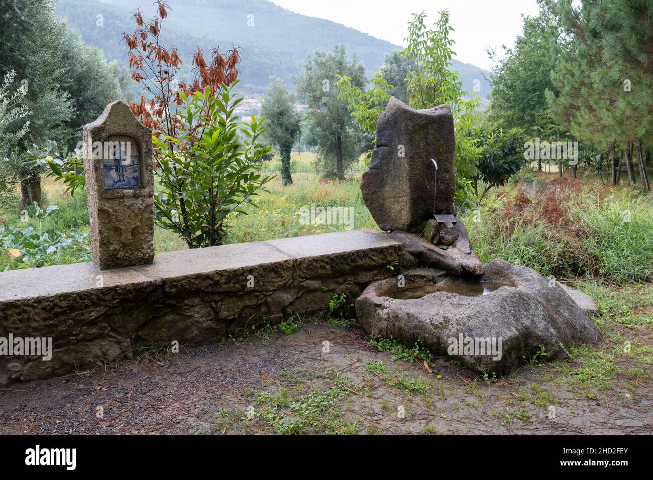 Una fontana rustica in pietra con un cartello segnaletico “água não controlada” lungo il Camino portoghese a Vitorino dos Piães, Portogallo. Questo percorso Foto Stock