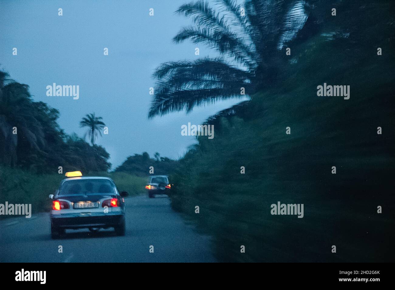 Vista posteriore di due taxi sulla strada in Congo al crepuscolo con palme. Ritorno a Pointe-Noire. Foto Stock