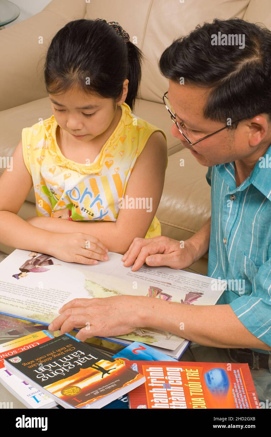 Famiglia vietnamita americana a casa, bambina di 8 anni che lavora alla lettura vietnamita, con suo padre Foto Stock