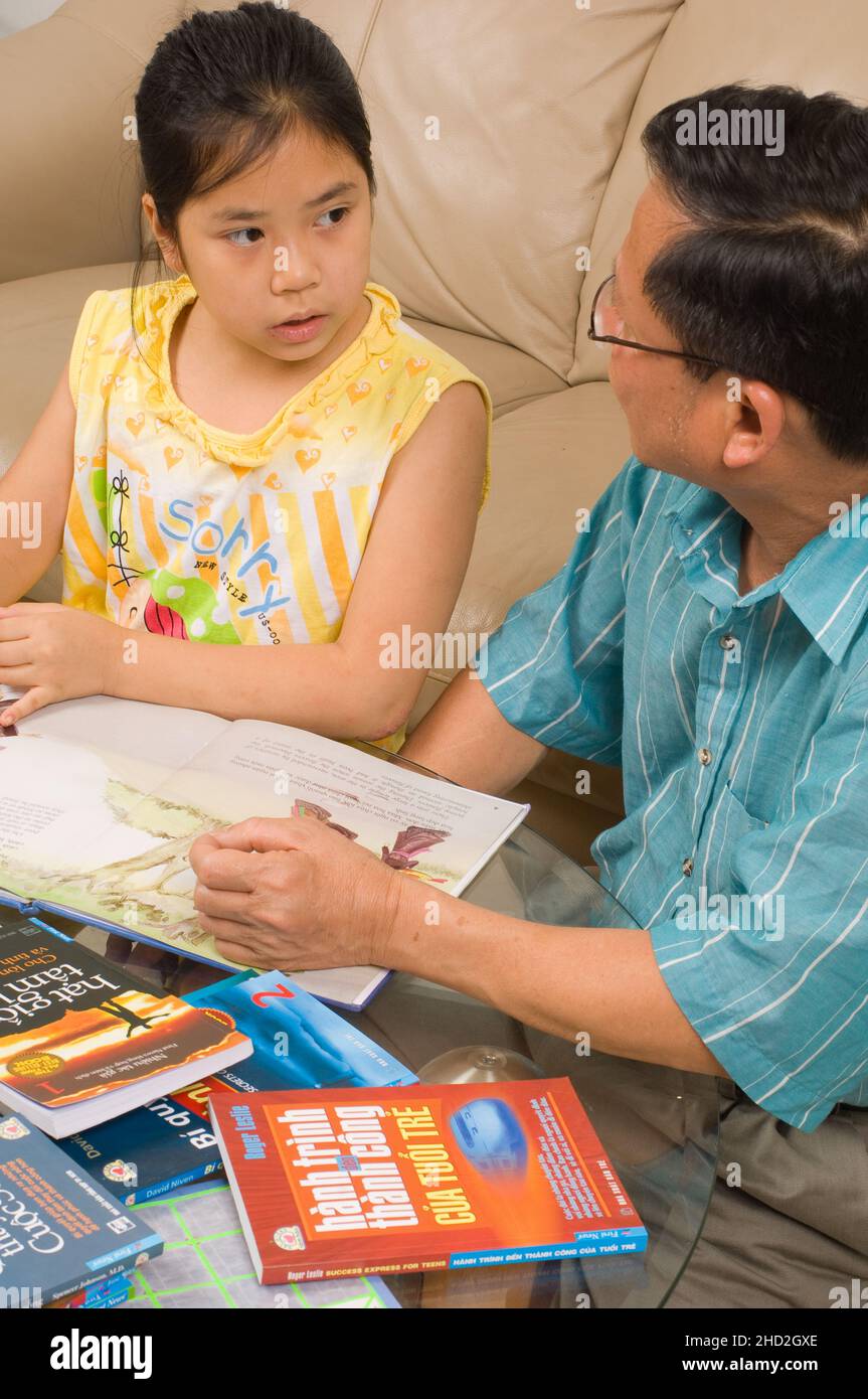 Famiglia vietnamita americana a casa, bambina di 8 anni che lavora alla lettura vietnamita, con suo padre Foto Stock
