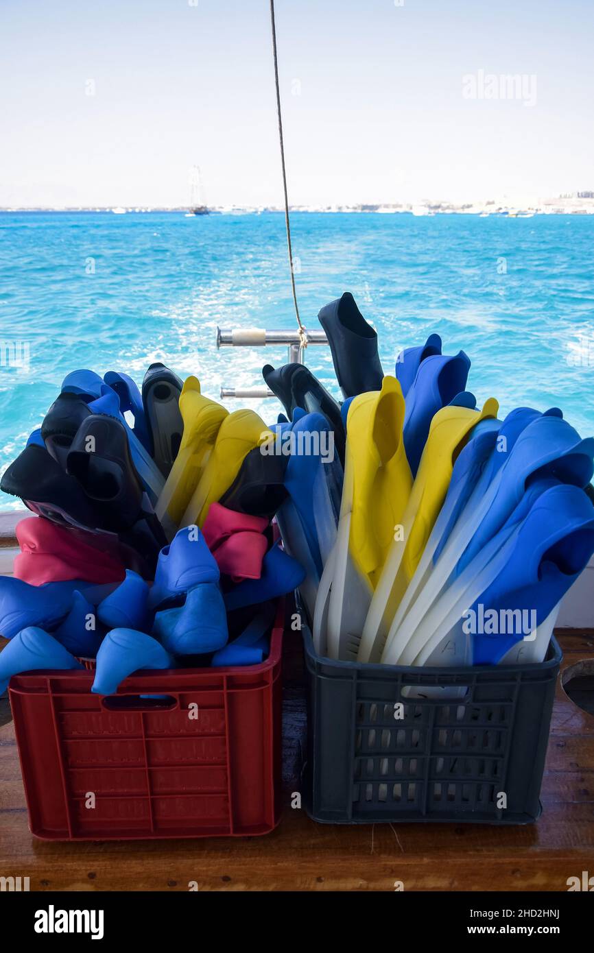 Le pinne multicolore in gomma per nuoto sono confezionate in scatole di plastica. Vista sullo sfondo di poppa di yacht e mare blu. Sentiero sull'acqua da Foto Stock