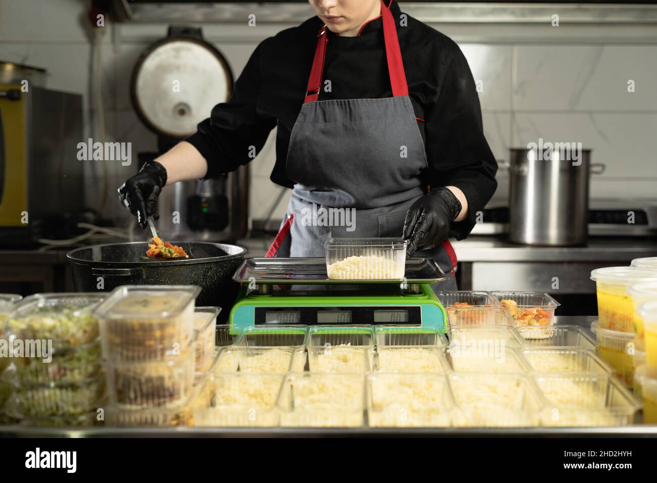 consegna del cibo al ristorante. mani di una donna chef in uniforme con guanti che pesano una porzione di riso su una bilancia elettronica. Piccola impresa Foto Stock