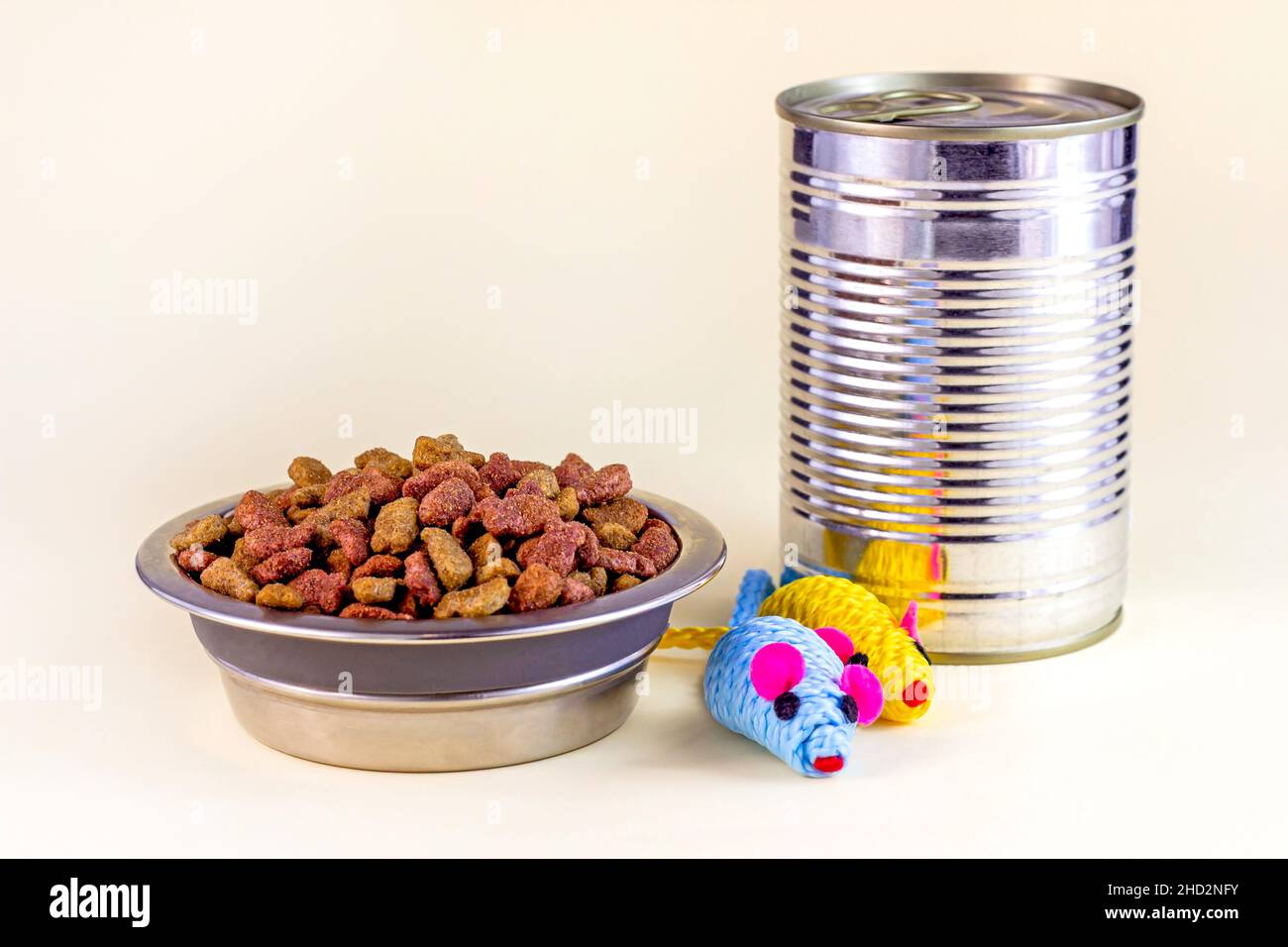Pezzi di kitty biologico croccante marrone in una ciotola, topi giocattolo e cibo umido gatto in lattina di metallo per l'alimentazione animale domestico su sfondo chiaro. Foto Stock