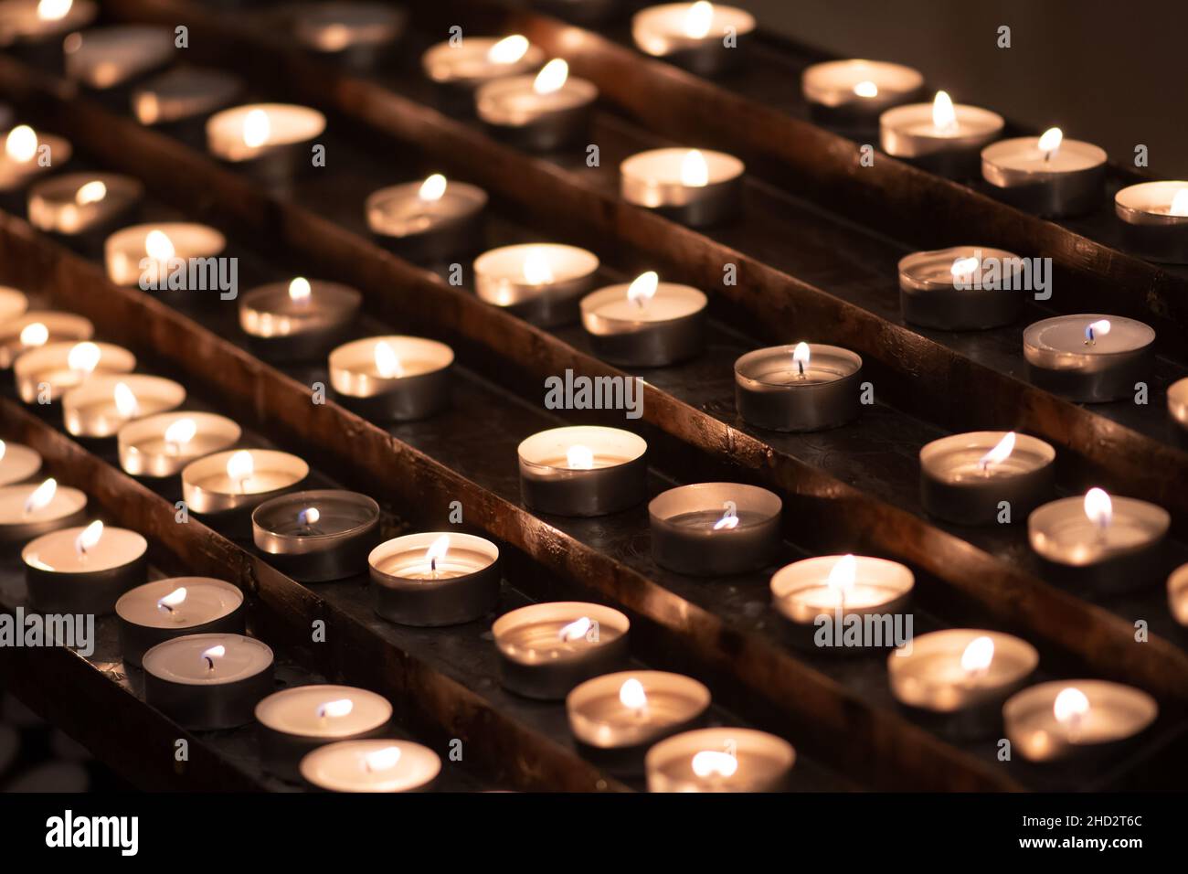 Molte candele in fila illuminano con una luce gialla dorata Foto Stock