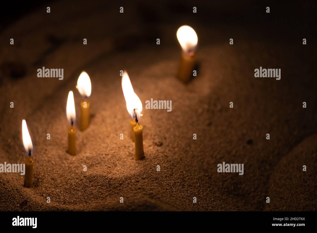 Candele sparse che illuminano con una luce gialla dorata nella sabbia, spazio copia Foto Stock