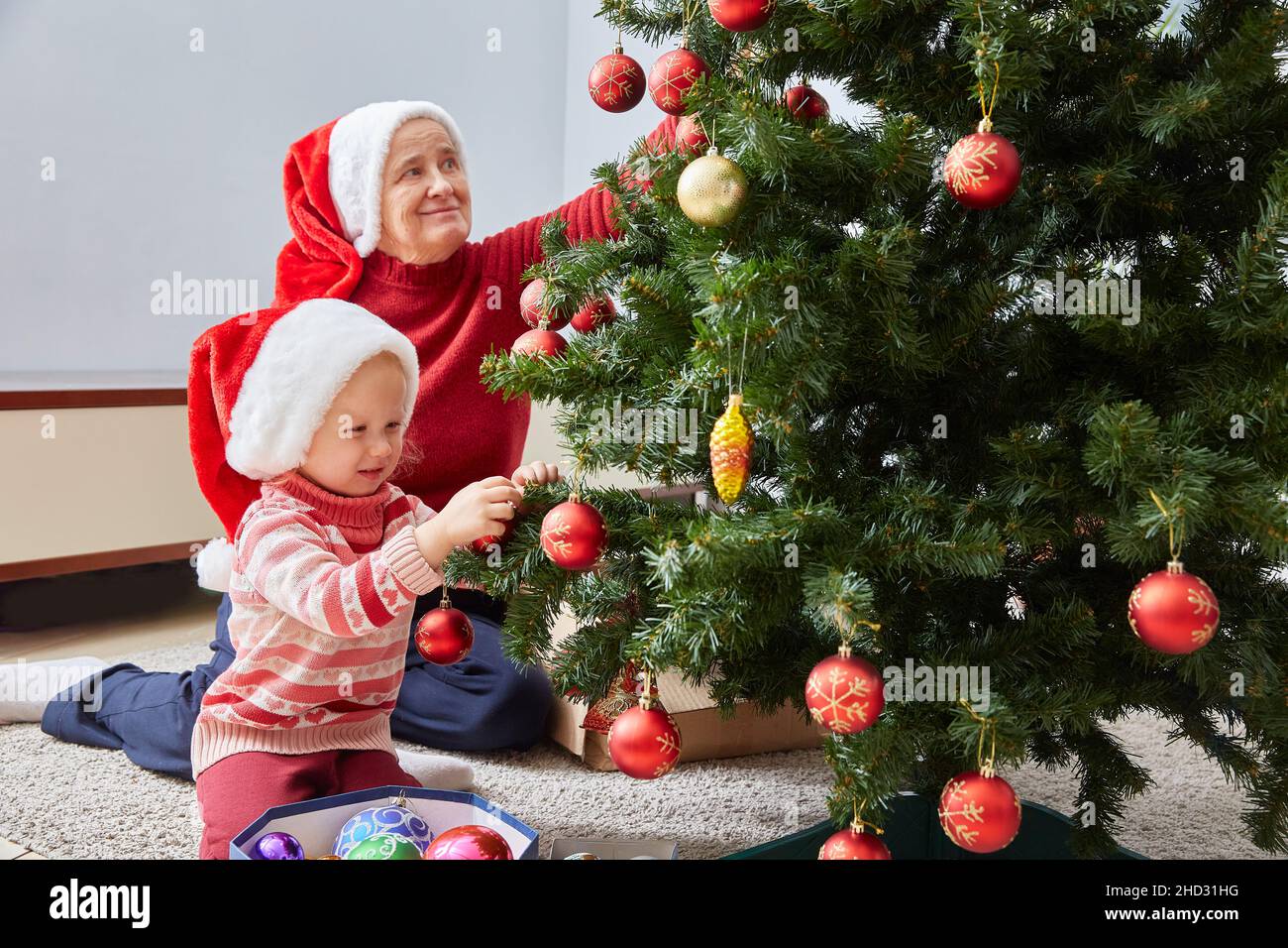 Buon Natale e buone feste. Felice nonna di famiglia e nipote decorare allegramente l'albero di Natale a casa. Una nonna e una piccola c Foto Stock