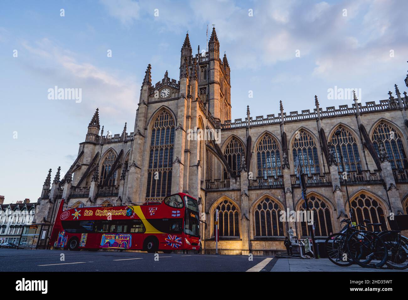 Tour in autobus rosso scoperto passando per la facciata gotica medievale dell'Abbazia di Bath nella storica città di Bath, Somerset, Inghilterra, Regno Unito, Patrimonio dell'Umanità Foto Stock