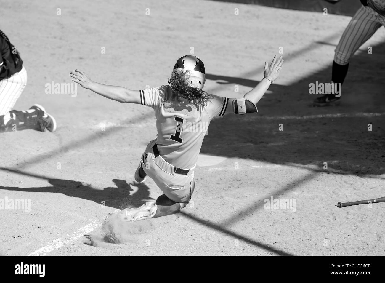 Un giocatore di baseball sta scivolando in Home Plate per battere la Throw Home e segnare Una corsa in un'immagine in bianco e nero Foto Stock