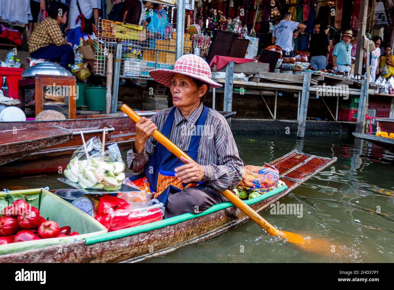 Thailandese lady barca operatore con il cibo nelle sue file di barche oltre un gruppo di persone nella parte di terra di sfondo del mercato. Foto Stock